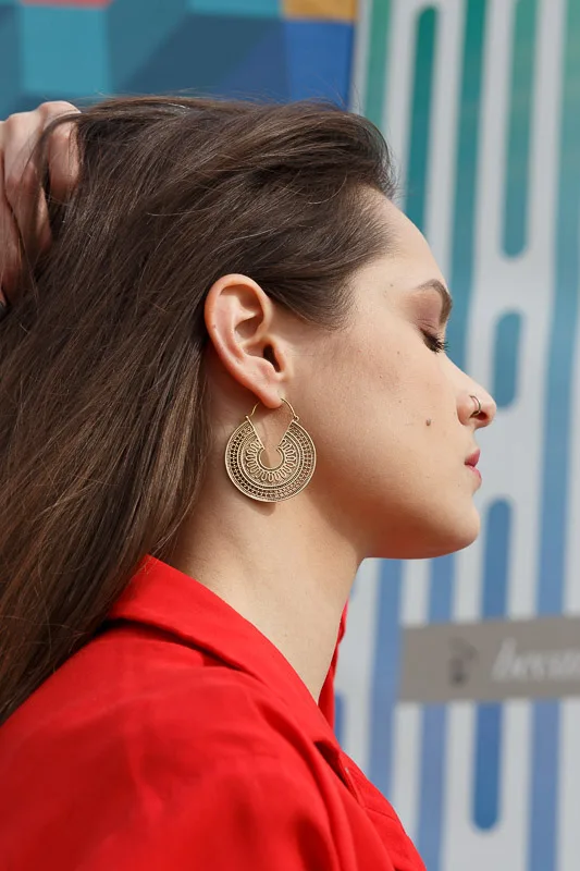 Photo of a Female model wearing Taksim Earrings Brass from Kiwa jewelry against a blue green wall